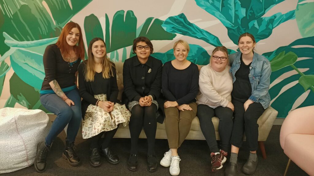 Six people sitting next to each other on a couch and smiling. The six people are all staff from the Inclusion Australia project team.