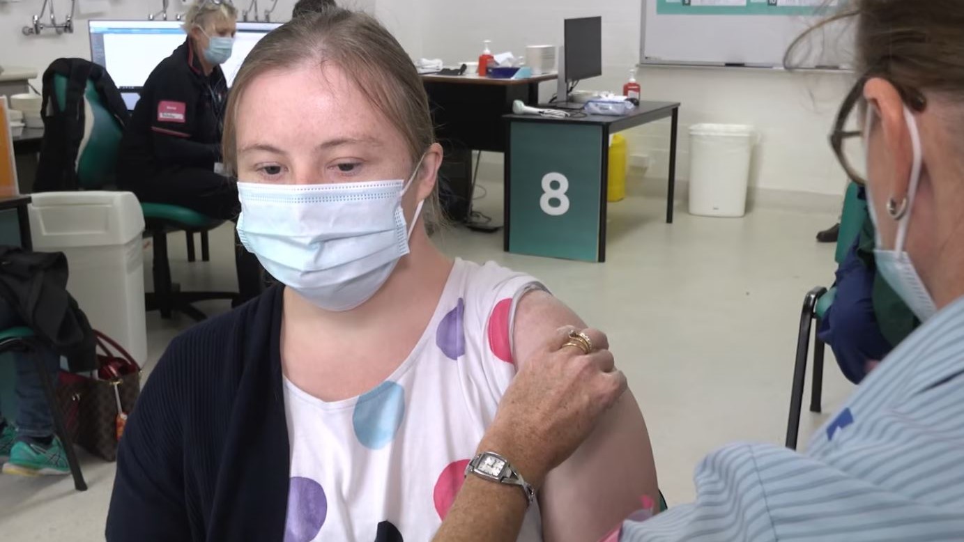 A woman wearing a face mask receiving a vaccination injection in her shoulder.